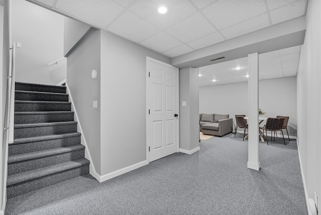 finished basement featuring a paneled ceiling, carpet floors, stairway, baseboards, and visible vents