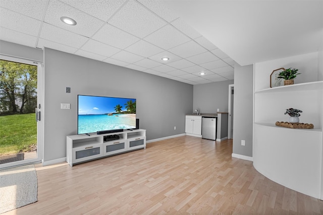 unfurnished living room featuring recessed lighting, light wood-style flooring, a paneled ceiling, baseboards, and bar area