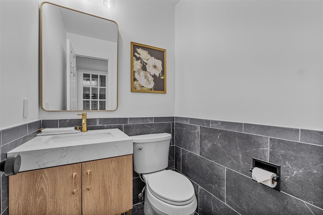 half bathroom with a wainscoted wall, vanity, tile walls, and toilet