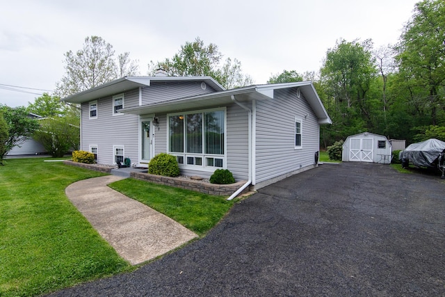 split level home with a storage unit, a chimney, a front yard, an outdoor structure, and asphalt driveway