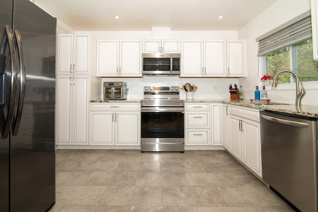 kitchen featuring stainless steel appliances, a sink, light stone counters, white cabinetry, and recessed lighting