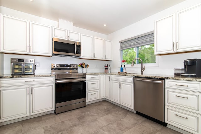 kitchen with stainless steel appliances, a sink, light stone countertops, white cabinetry, and recessed lighting