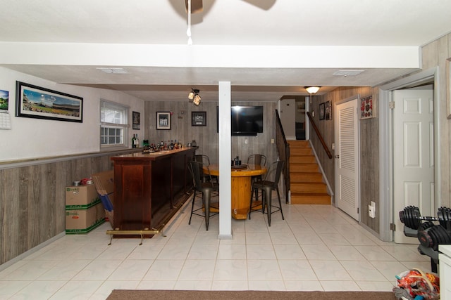 indoor dry bar with wood walls, stairway, wainscoting, and light tile patterned floors
