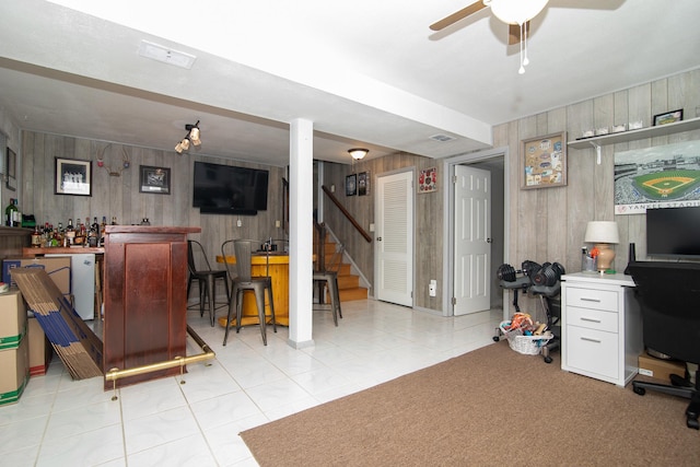 home office with wood walls, a dry bar, a ceiling fan, and light tile patterned floors