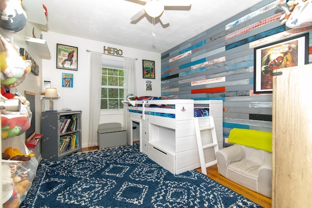 bedroom with wood finished floors, wood walls, and a ceiling fan