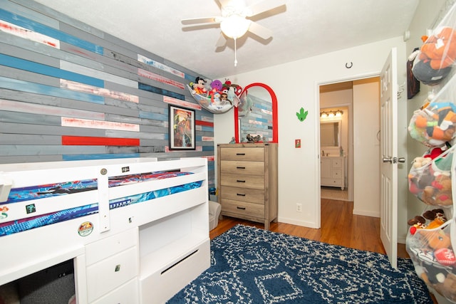 bedroom with wood finished floors, wooden walls, a ceiling fan, and baseboards