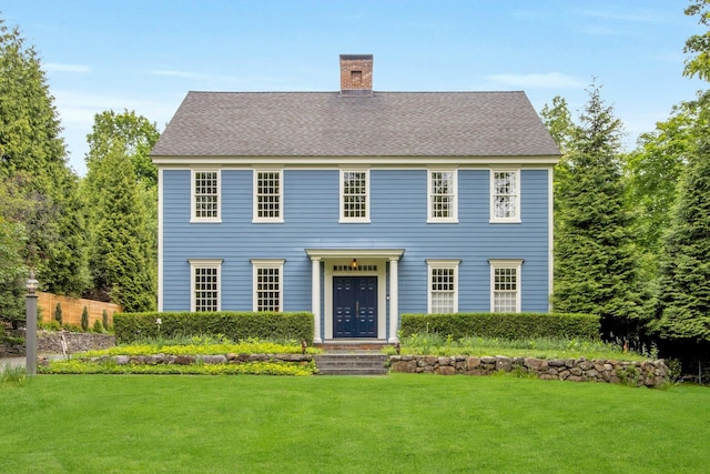 colonial house featuring a chimney, a front lawn, and a shingled roof