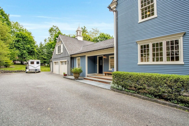 view of front of property featuring asphalt driveway, covered porch, roof with shingles, and a chimney