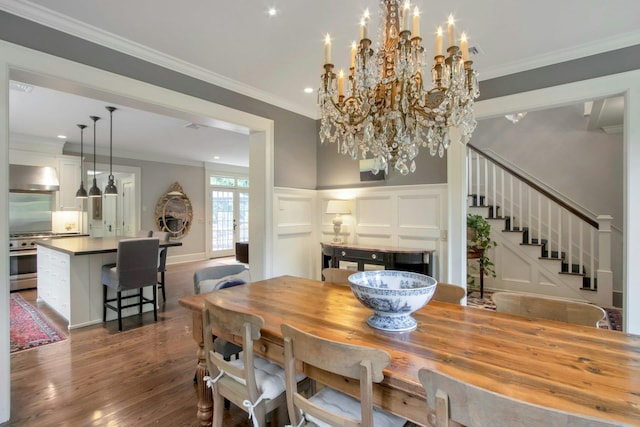 dining space featuring a decorative wall, dark wood-type flooring, stairs, crown molding, and a wainscoted wall