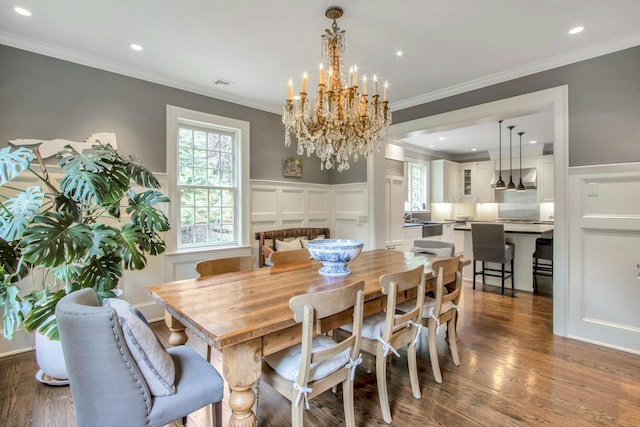 dining area with wood finished floors, a chandelier, a decorative wall, ornamental molding, and a wainscoted wall