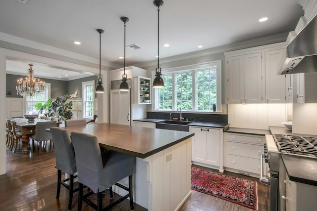 kitchen with a sink, dark countertops, wall chimney range hood, dark wood finished floors, and high end stove