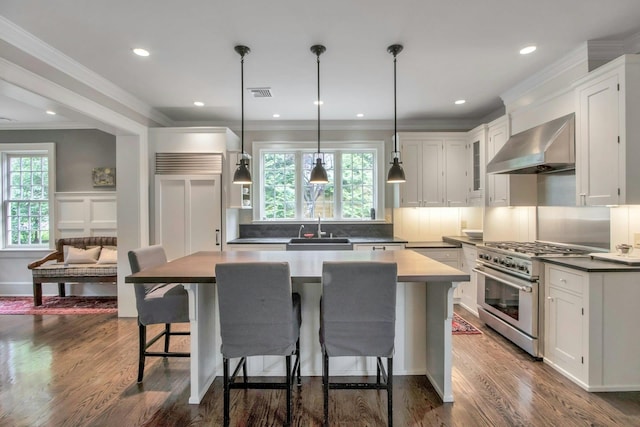 kitchen featuring wall chimney exhaust hood, high end stove, a sink, a breakfast bar, and plenty of natural light
