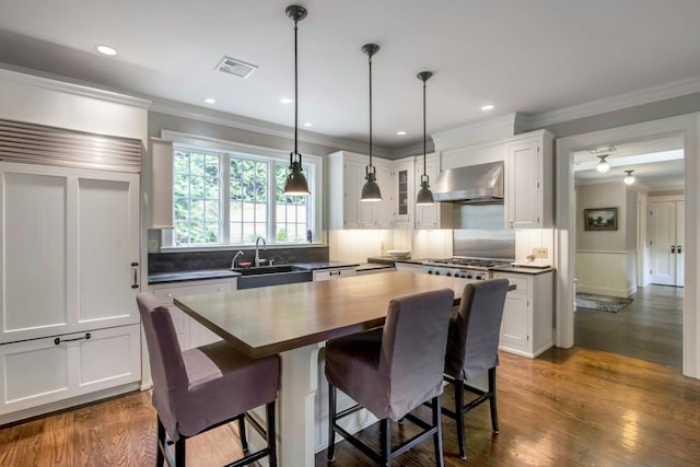kitchen with wall chimney exhaust hood, a sink, ornamental molding, a breakfast bar, and white cabinetry