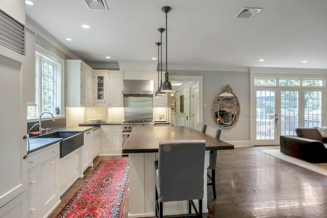 kitchen with a sink, crown molding, dark countertops, a kitchen bar, and dark wood finished floors