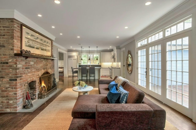 living room with crown molding, wood finished floors, recessed lighting, and a brick fireplace