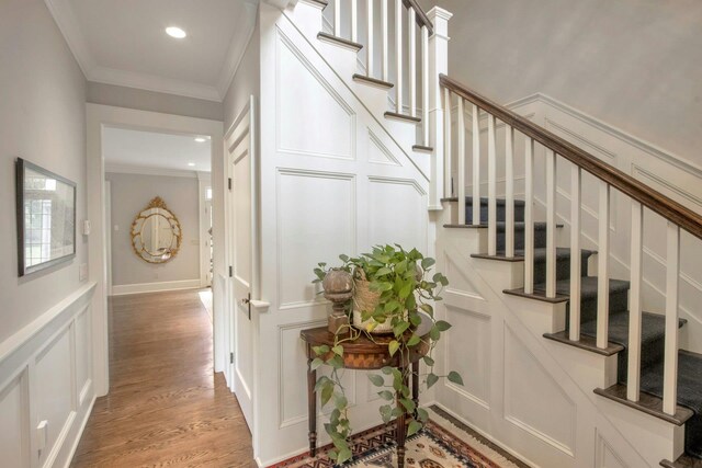 stairs featuring ornamental molding, wood finished floors, recessed lighting, and a decorative wall
