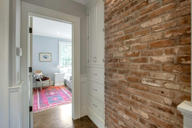 hall featuring dark wood-style floors, ornamental molding, and brick wall