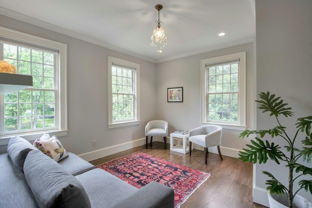 sitting room featuring healthy amount of natural light, crown molding, wood finished floors, baseboards, and a chandelier
