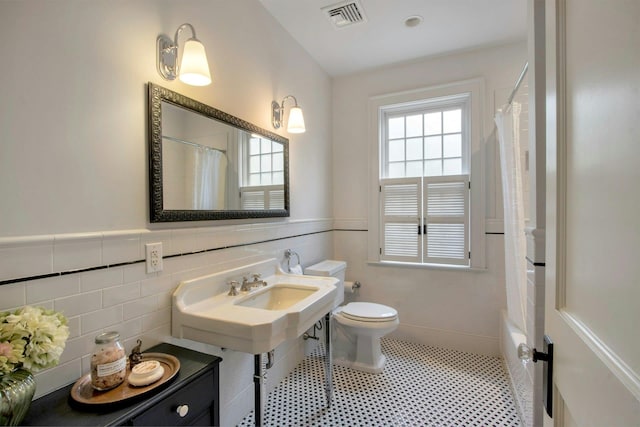 bathroom featuring toilet, tile walls, and a wainscoted wall