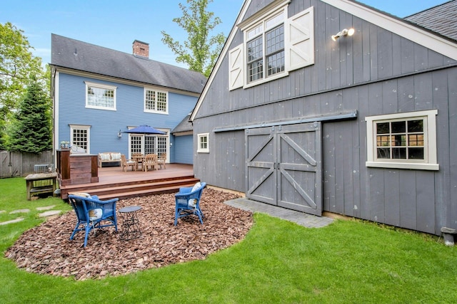 back of house with a barn, a deck, a lawn, and an outbuilding