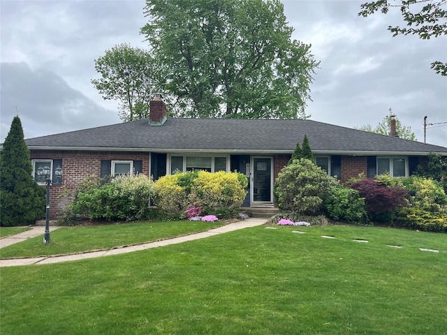 ranch-style home featuring brick siding, a front yard, and a chimney