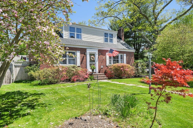 view of front of home featuring a chimney, fence, a front lawn, brick siding, and roof with shingles