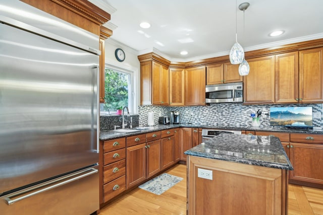 kitchen with a sink, brown cabinetry, crown molding, a kitchen island, and appliances with stainless steel finishes