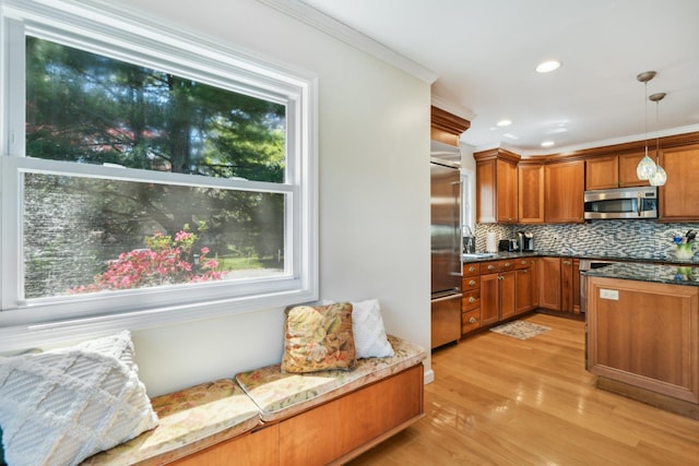 kitchen with ornamental molding, brown cabinetry, a healthy amount of sunlight, and appliances with stainless steel finishes
