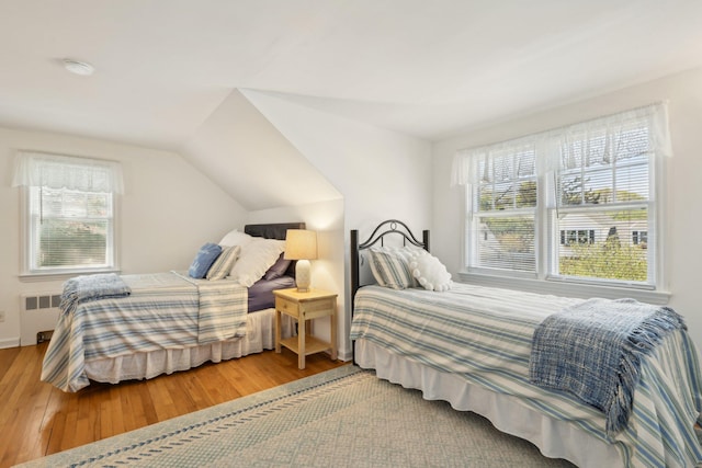 bedroom with multiple windows, wood finished floors, and radiator heating unit