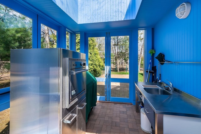 kitchen featuring french doors, refrigerator, a sink, stainless steel countertops, and brick floor