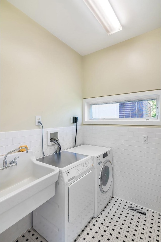 laundry area featuring a sink, tile walls, a wainscoted wall, independent washer and dryer, and laundry area