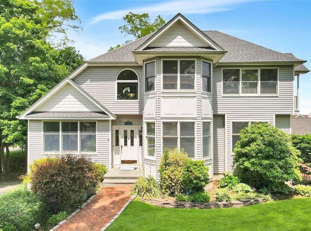 view of front of home with roof with shingles and a front yard