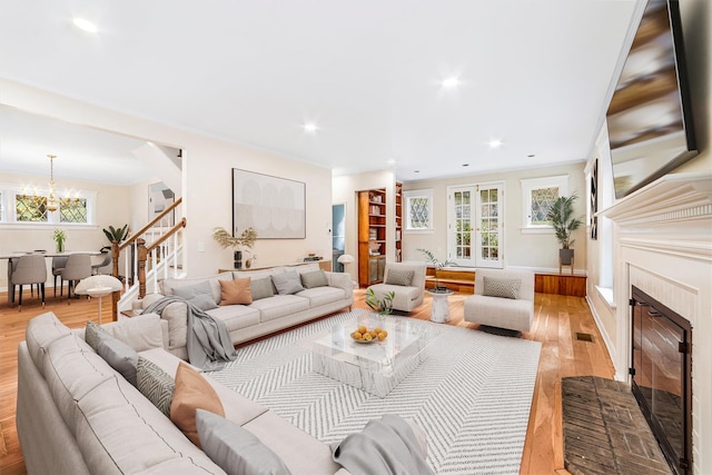 living room with stairs, wood finished floors, recessed lighting, a chandelier, and a glass covered fireplace