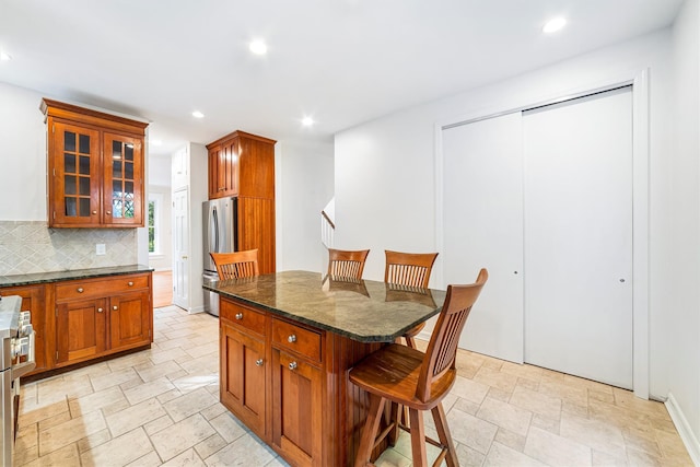 kitchen featuring a kitchen bar, freestanding refrigerator, stone finish floor, tasteful backsplash, and recessed lighting