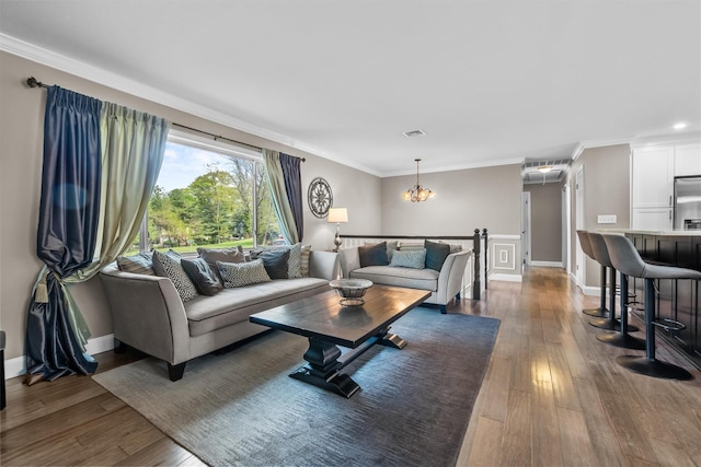 living area with a notable chandelier, baseboards, visible vents, wood-type flooring, and crown molding