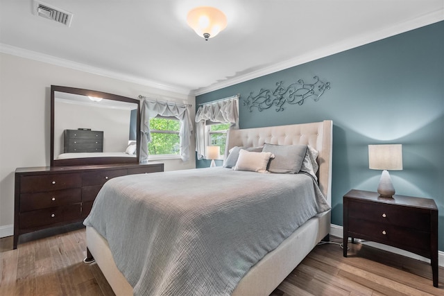 bedroom with baseboards, crown molding, visible vents, and wood finished floors