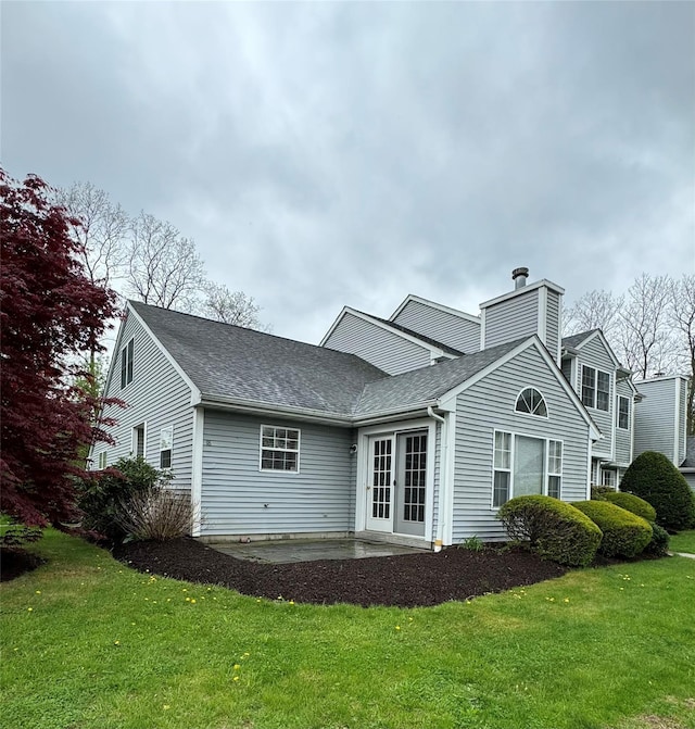 rear view of house featuring roof with shingles, french doors, a patio, a chimney, and a lawn