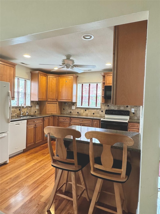 kitchen featuring white appliances, a sink, decorative backsplash, a ceiling fan, and healthy amount of natural light