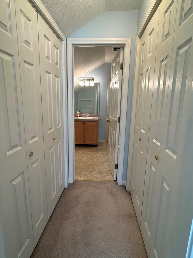 corridor with a textured ceiling, lofted ceiling, light tile patterned floors, light colored carpet, and baseboards