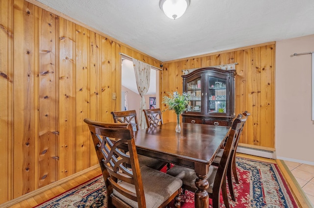 dining room featuring a baseboard heating unit, wooden walls, baseboards, and a textured ceiling