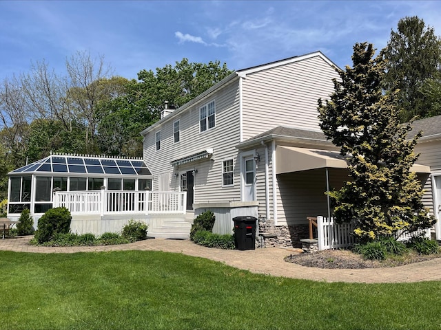 rear view of house featuring a yard, a wooden deck, and a sunroom