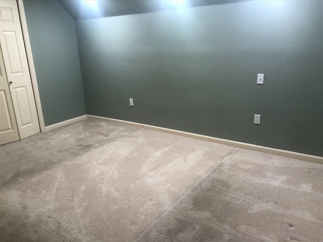 carpeted empty room featuring baseboards and vaulted ceiling