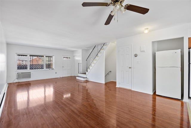 unfurnished living room with ceiling fan, a wall mounted AC, wood finished floors, and stairway