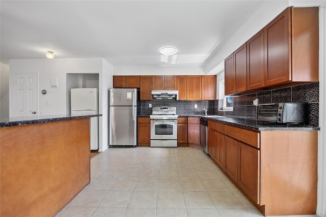 kitchen with decorative backsplash, appliances with stainless steel finishes, a toaster, dark stone countertops, and under cabinet range hood