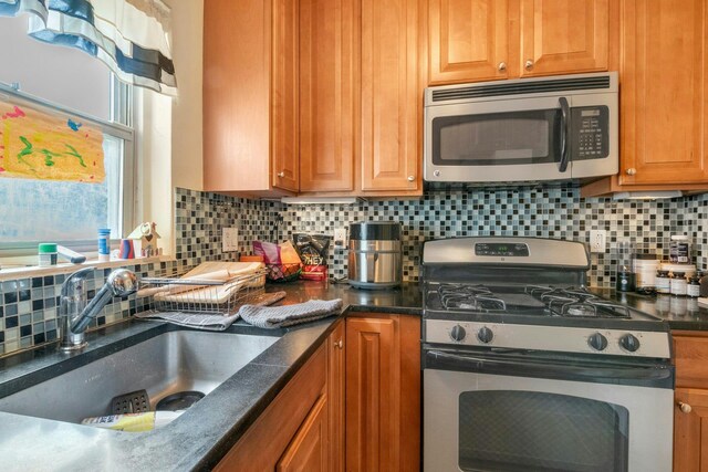 kitchen featuring a sink, stainless steel appliances, backsplash, and brown cabinets