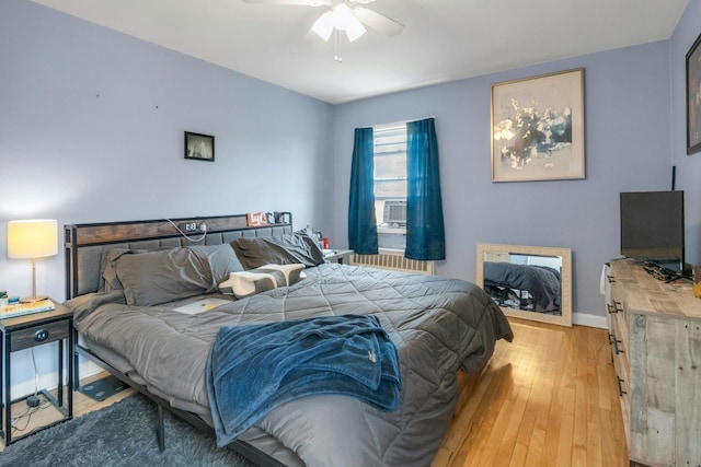 bedroom featuring a ceiling fan, cooling unit, baseboards, light wood-style floors, and radiator heating unit