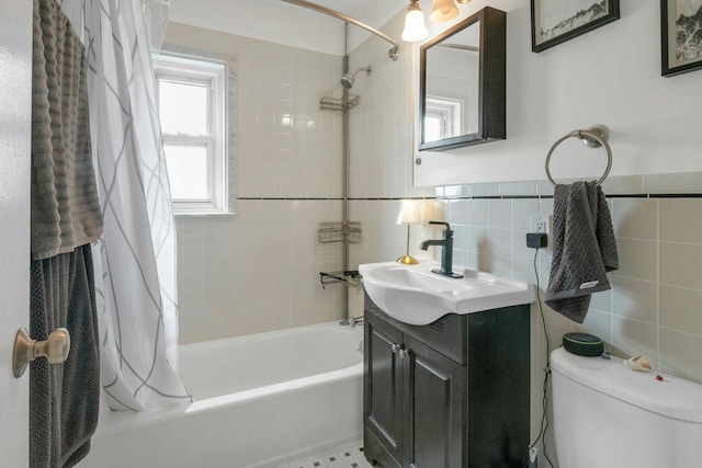 bathroom with tile walls, shower / bath combo with shower curtain, toilet, vanity, and a wainscoted wall