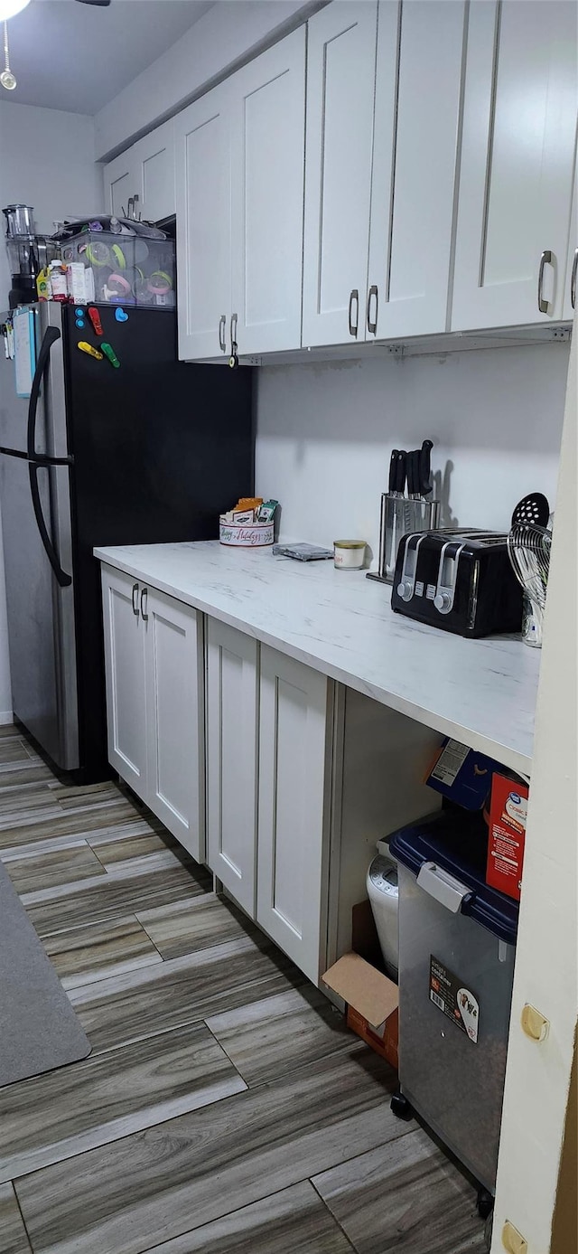 kitchen with freestanding refrigerator, white cabinetry, and light stone countertops