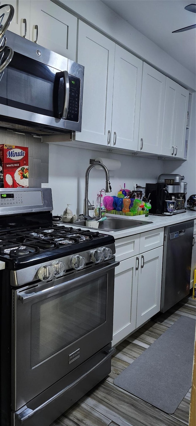 kitchen with wood finished floors, a sink, light countertops, white cabinets, and stainless steel appliances