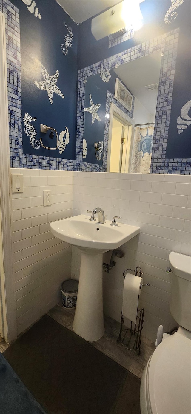 bathroom featuring a sink, wainscoting, toilet, and tile walls